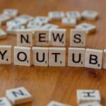 Scrabble tiles spelling words on wooden surface, focusing on YouTube and News.