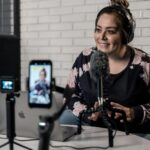 Woman recording video podcast with microphone and camera setup in modern studio.